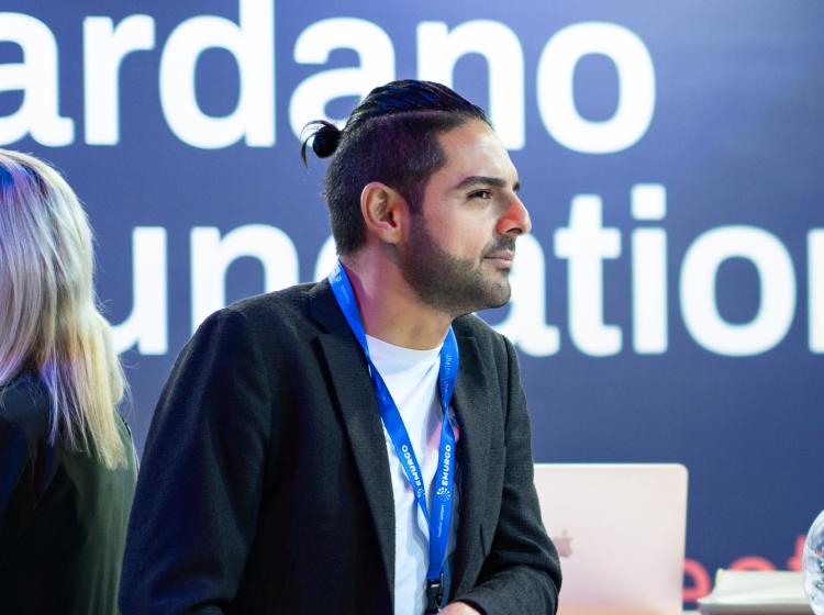 A photograph of an individual engaged in a discussion at the Cardano Foundation booth. 